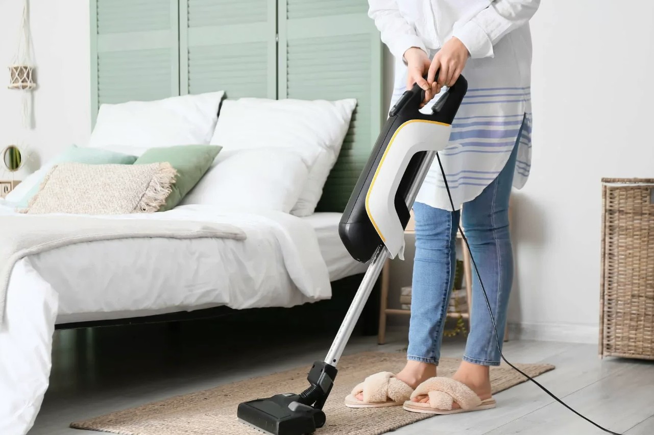 A cleaner vacuuming a bright, tidy bedroom